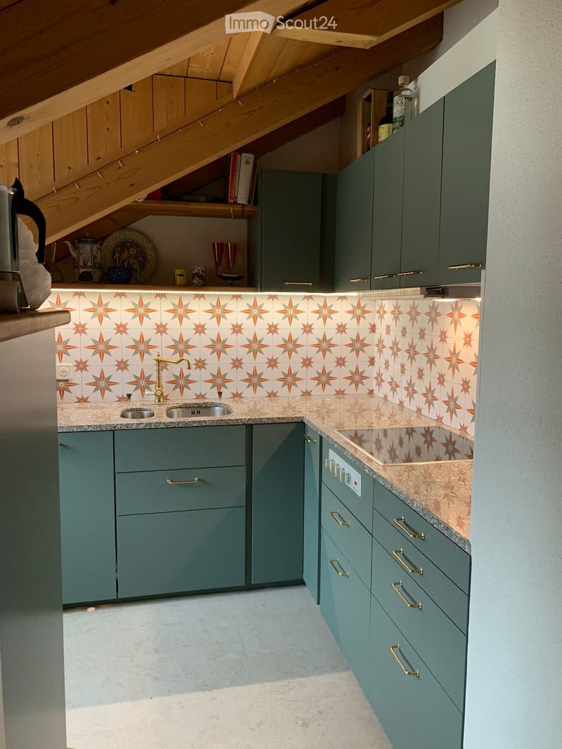 Modern kitchen with teal cabinets, marble countertops, and a decorative backsplash featuring orange star patterns. Includes a sink, faucet, and various kitchen items on the counter and shelves.