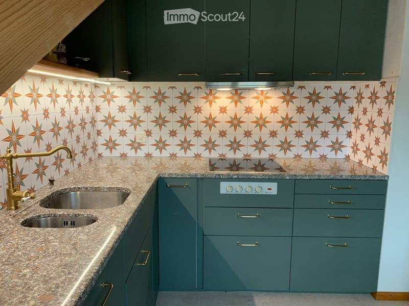 Modern kitchen with granite countertops, stainless steel sink, brass faucet, and grey cabinets.
