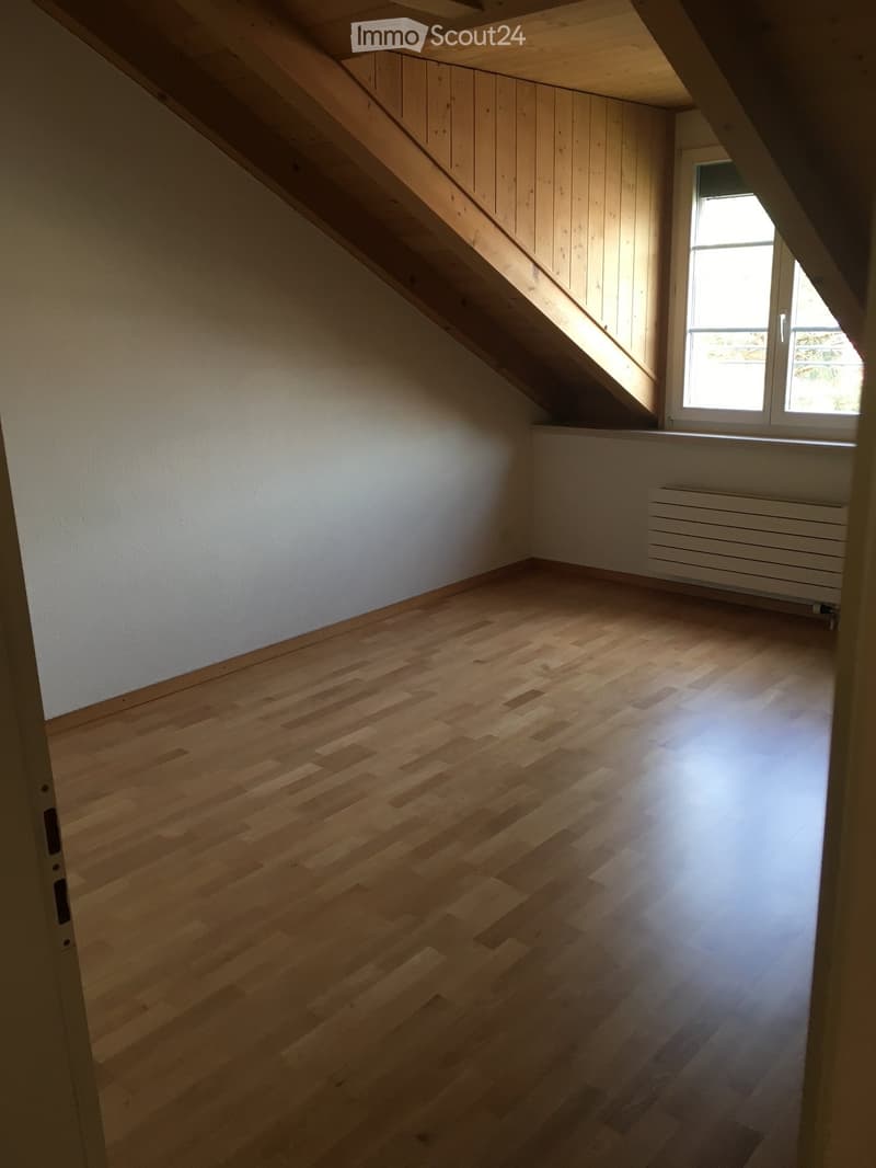 Empty attic room with wooden flooring, white walls, and a window letting in natural light. No furniture or equipment is present.
