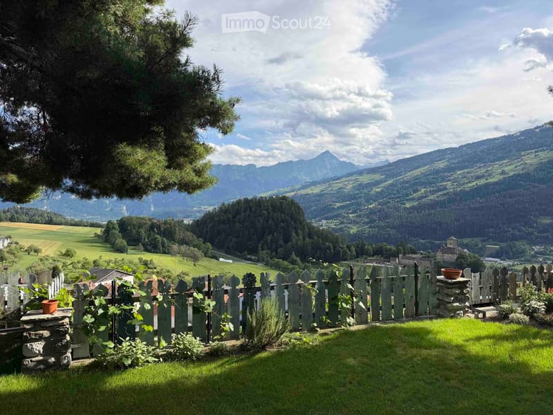A serene garden area with a wooden fence, lush green grass, and a scenic mountain view in the background.