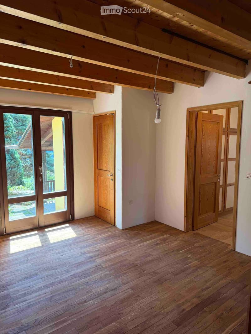 Empty room with wooden floor, exposed wooden beams on the ceiling, and several wooden doors leading to other spaces.