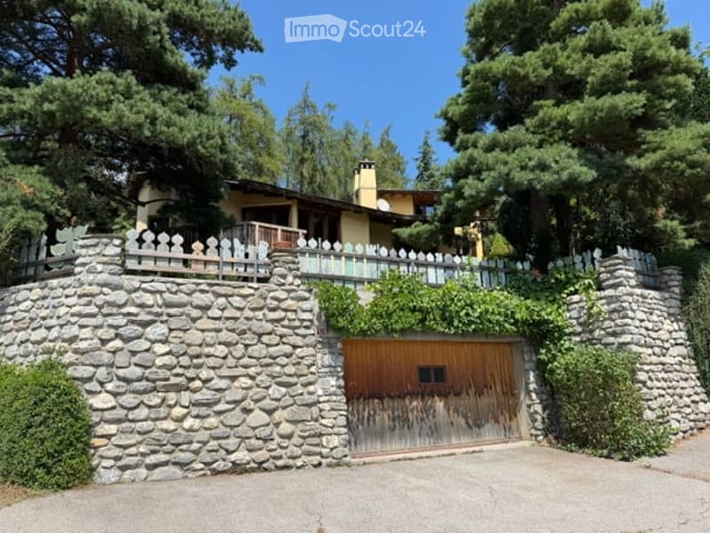 A two-story house with a stone retaining wall, wooden garage door, and white picket fence on the balcony.