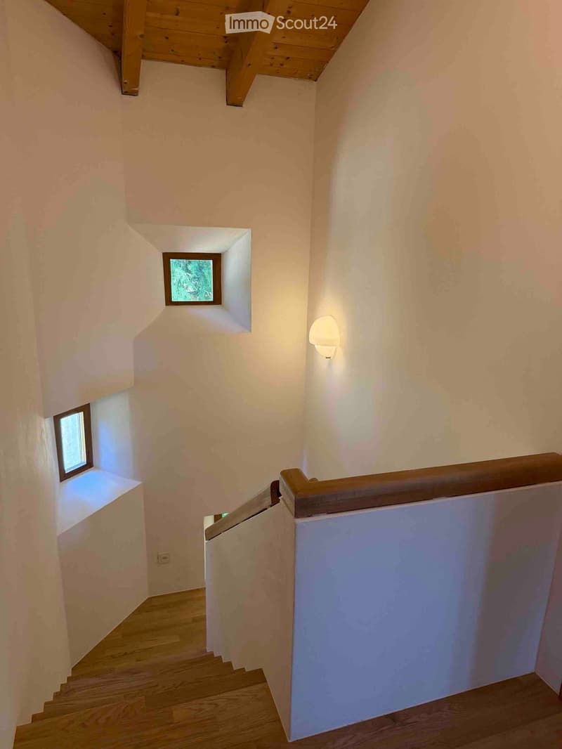 Wooden staircase with white walls, small windows, and a wall-mounted light fixture.