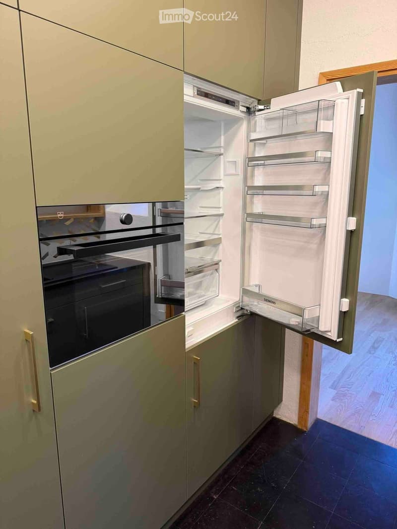 Modern kitchen with light-colored cabinets, an open refrigerator, and a built-in oven.