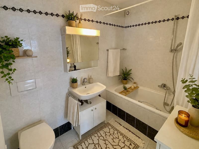 Modern bathroom with white tiles, a sink with a mirror cabinet, a toilet, a bathtub, and decorative plants and candles.