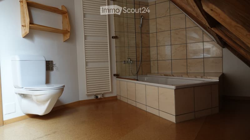 Modern bathroom with a toilet, bathtub, and a glass-enclosed shower. Features wooden shelves and a sleek, contemporary design.