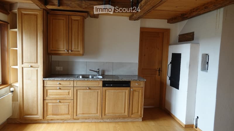 Compact kitchen with light wooden cabinets, granite countertop, sink, dishwasher, and refrigerator. Wooden floor and exposed wooden beams on the ceiling.
