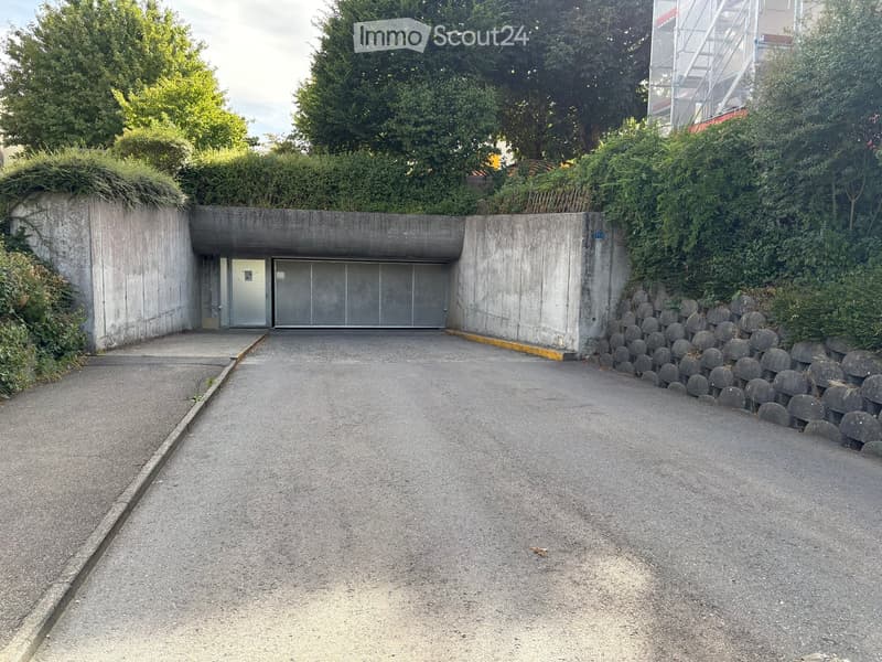 A concrete garage entrance with a raised ground floor, surrounded by greenery and a stone wall.