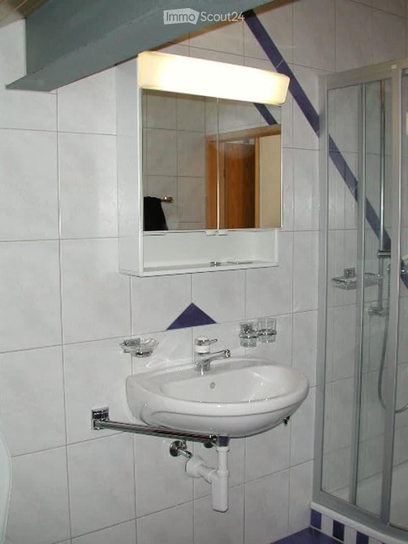 Modern bathroom with white tiled walls, a white sink with a chrome faucet, a mirrored medicine cabinet above, and a glass-enclosed shower stall.
