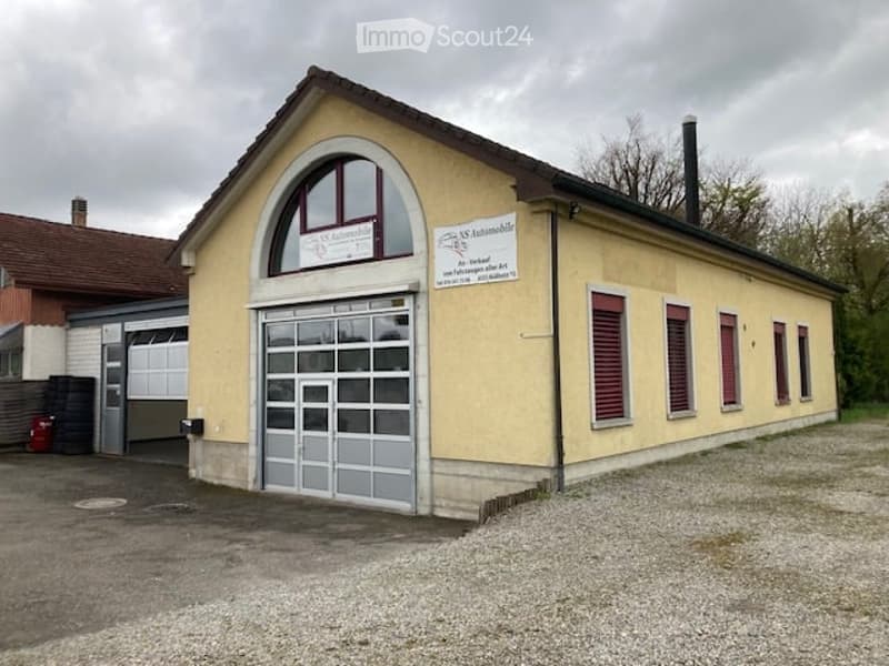 Single-story building with a garage entrance, yellow facade, arched window above the door, and signage on the wall.