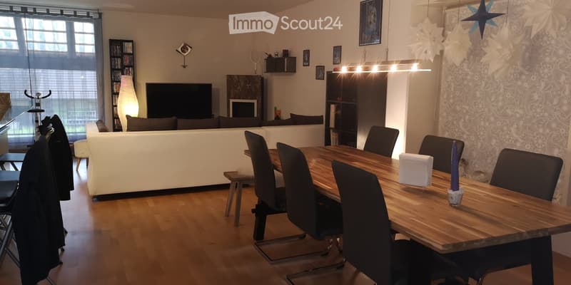 Modern living and dining area with a white sofa, wooden dining table, chairs, a TV, and decorative items including a lamp and candle.