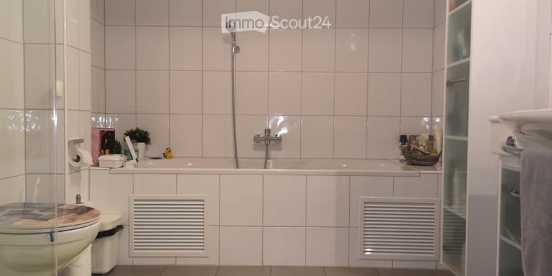 Modern bathroom with white tiles, bathtub, toilet, sink, and shower. Includes a small plant and decorative items on the bathtub ledge.