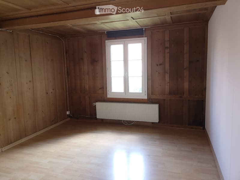 Empty room with wooden walls, wooden floor, white radiator, and a window with white frame.