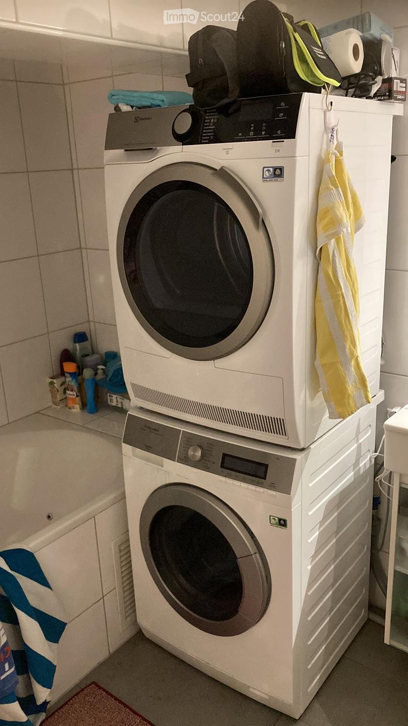 Bathroom with a stacked washing machine and dryer, towels, and a backpack on top.