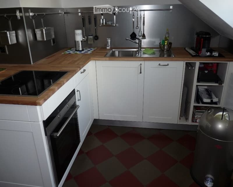 Modern kitchen with white cabinets, wooden countertops, and stainless steel appliances. Features include a sink, oven, microwave, and refrigerator, with a checkered floor.