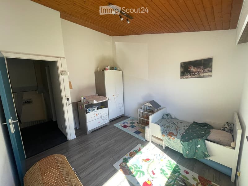 Child's bedroom with a white wooden bed, a wardrobe, a changing table, a toy house, a shelf, and a picture frame on the wall.