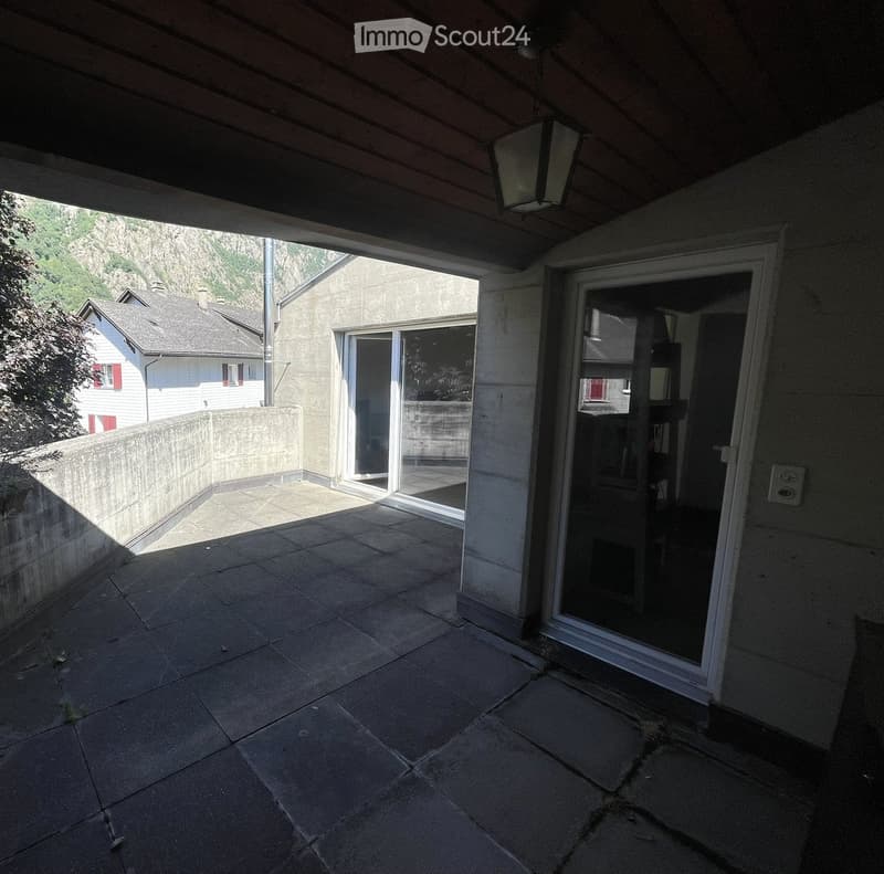 Balcony with tiled floor, glass sliding doors, and a view of a stone wall and neighboring house.