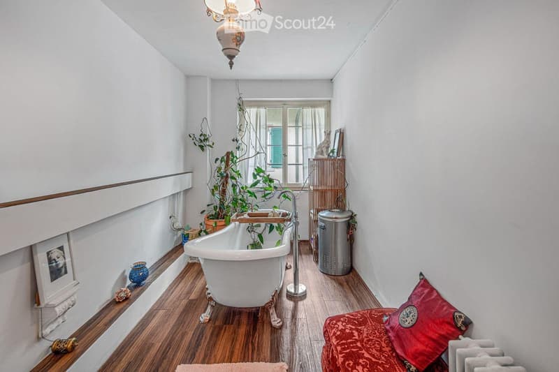 white bathtub, wooden floor, white walls, fireplace, plants, radiator, picture frame, trash can