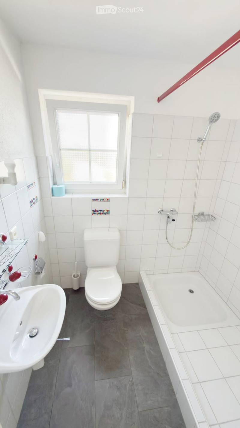 Modern bathroom with white tiles, a toilet, a sink, a bathtub, and a shower. Features a window with frosted glass and a towel rack on the wall.