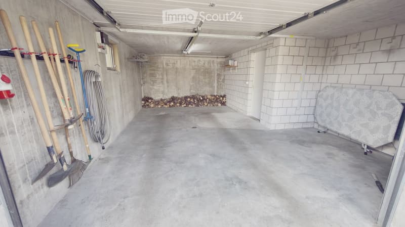 Empty garage with concrete floor, concrete walls, and storage space for tools and firewood.