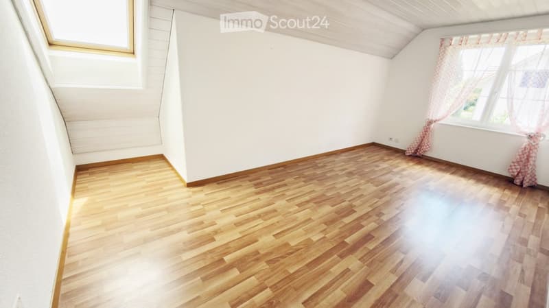 Empty room with wooden flooring, white walls, and large windows with curtains. No furniture or equipment present.