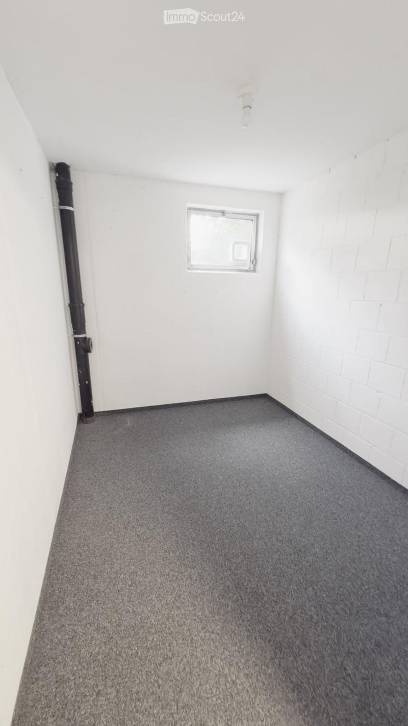 Empty room with white walls, grey carpet, and a small window. No furniture or equipment present.