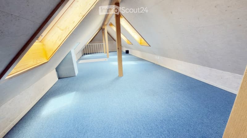 Empty attic space with blue carpeting, wooden beams, and skylights allowing natural light to enter.