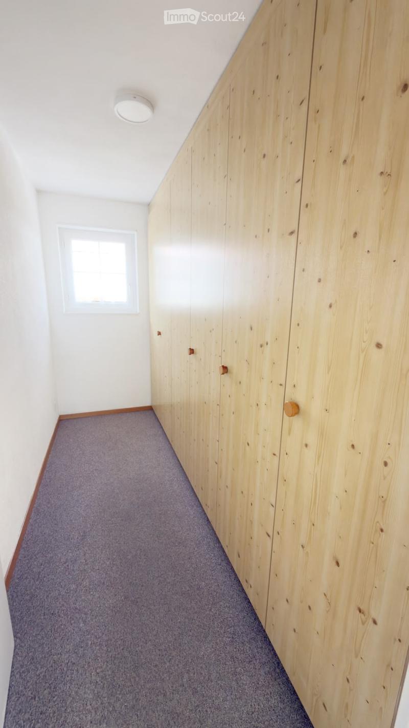 A narrow hallway with wooden panel walls, carpeted floor, and a small window on the left side.
