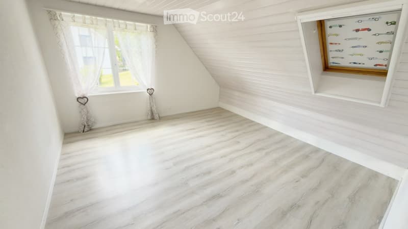 Empty attic room with white wooden walls, marble flooring, large windows with sheer curtains, and decorative heart-shaped wall hangings.