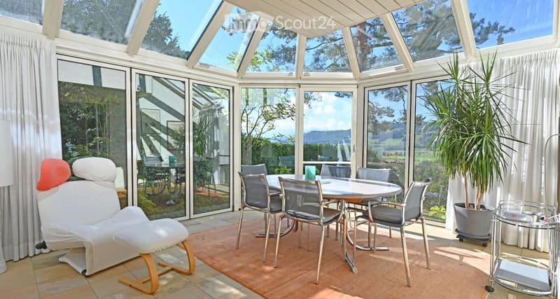 Furnished Room. Brightly lit room with large windows and a view, featuring a white sofa, a small dining table with chairs, and a potted plant.