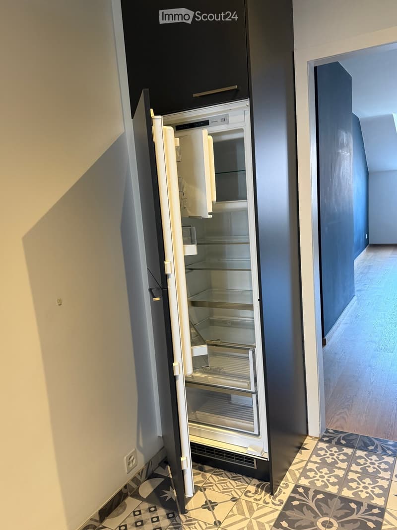 Open refrigerator with empty shelves and compartments, modern design, located in a kitchen with patterned tiles and wooden flooring.