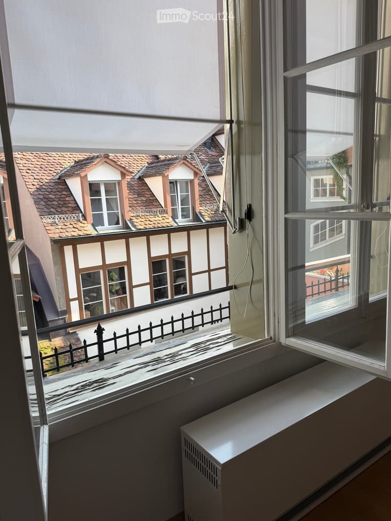 Balcony with metal railing, overlooking a traditional half-timbered house with red-tiled roof and white walls.