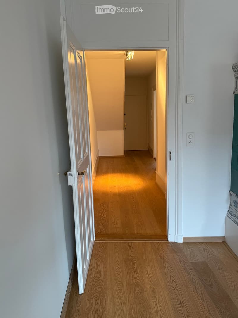 Empty hallway with wooden flooring, white walls, and a partially open door leading to another room.