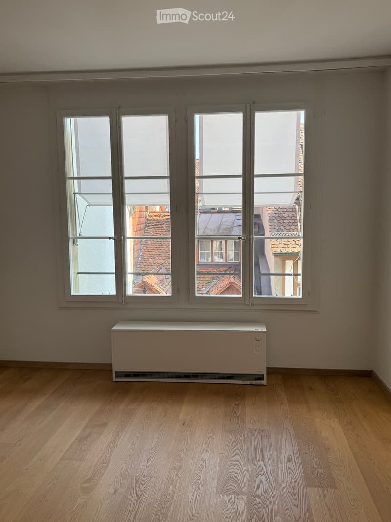 Empty room with wooden flooring, large windows, and a radiator under the windows.