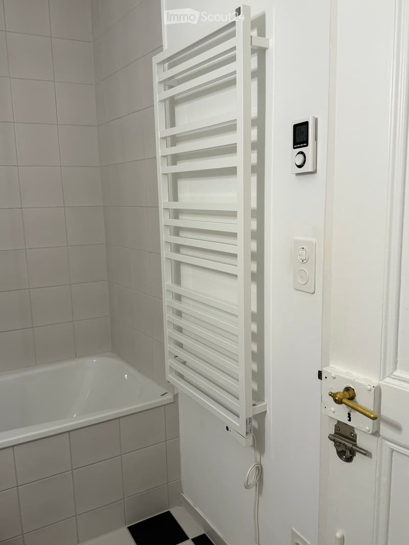 Bathroom with a bathtub, white radiator, and digital thermostat on the wall.