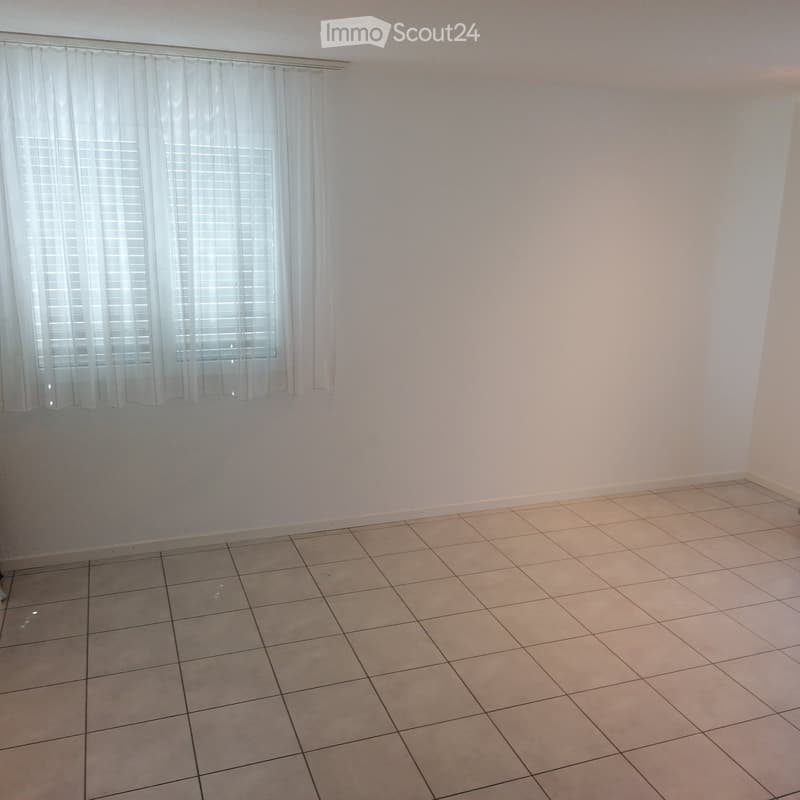 Empty room with tiled floor and white walls, featuring a window with white curtains.