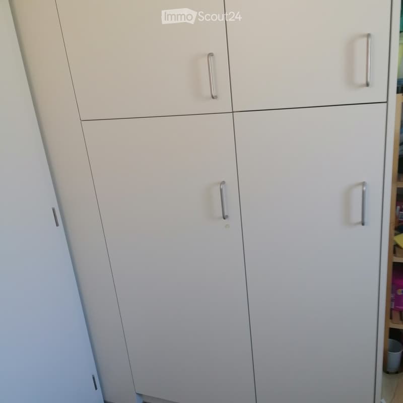 A modern, white wardrobe with multiple doors and silver handles, positioned against a wall in a room.