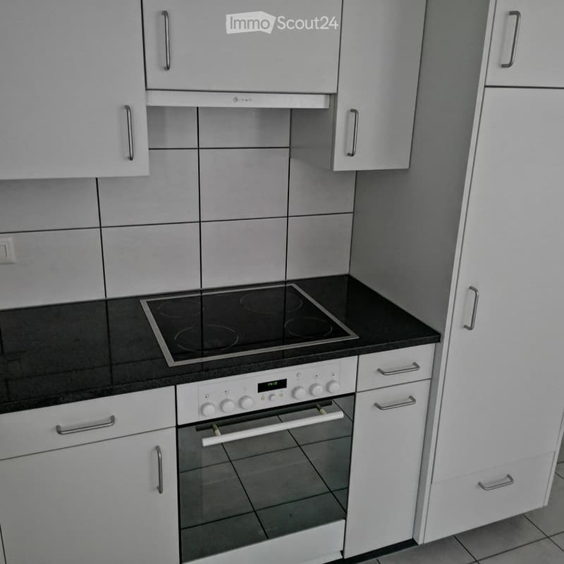 Modern kitchen with white cabinets, black countertop, induction cooktop, and built-in oven.