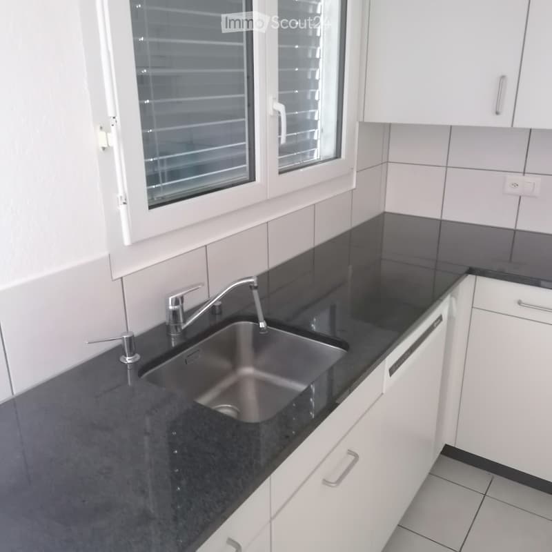 Modern kitchen with black countertops, white cabinets, and a stainless steel sink.