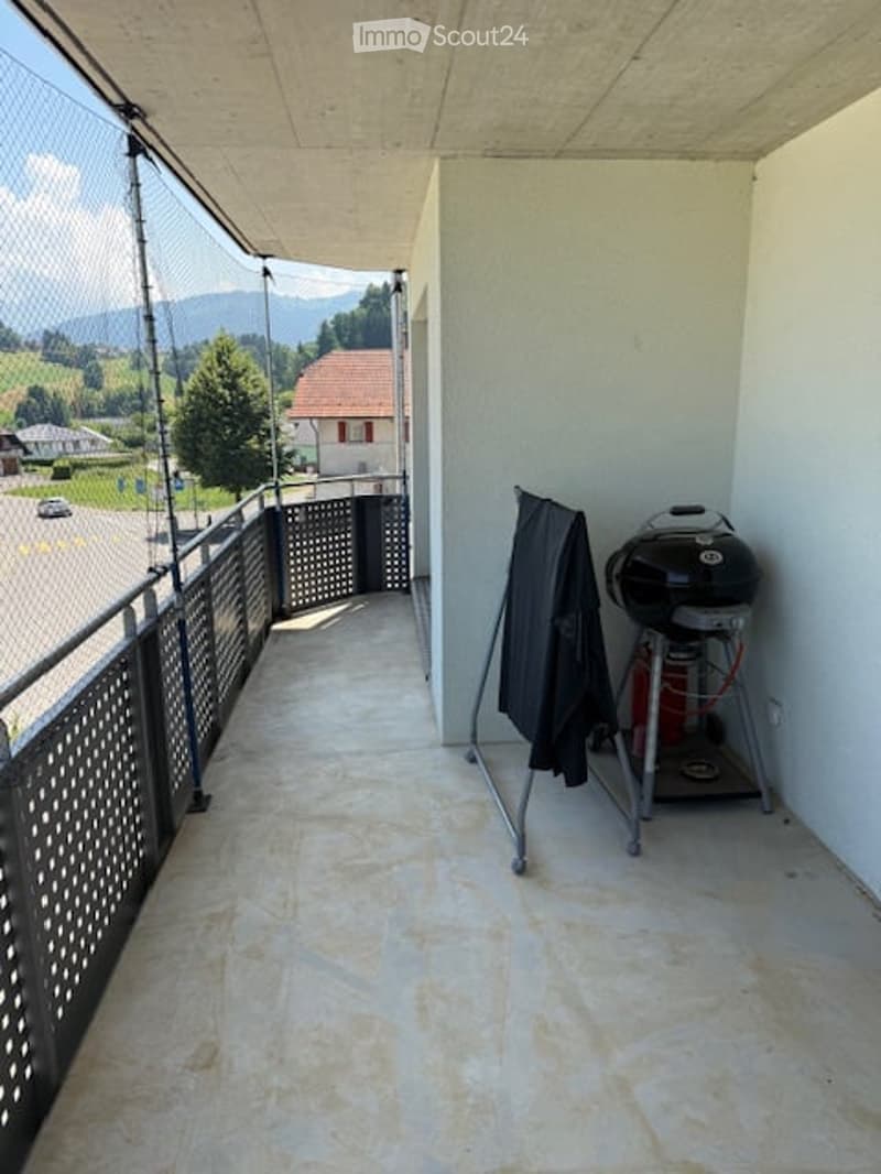 Balcony with a view of the surrounding landscape, featuring a metal railing, a grill, and a hanging jacket.
