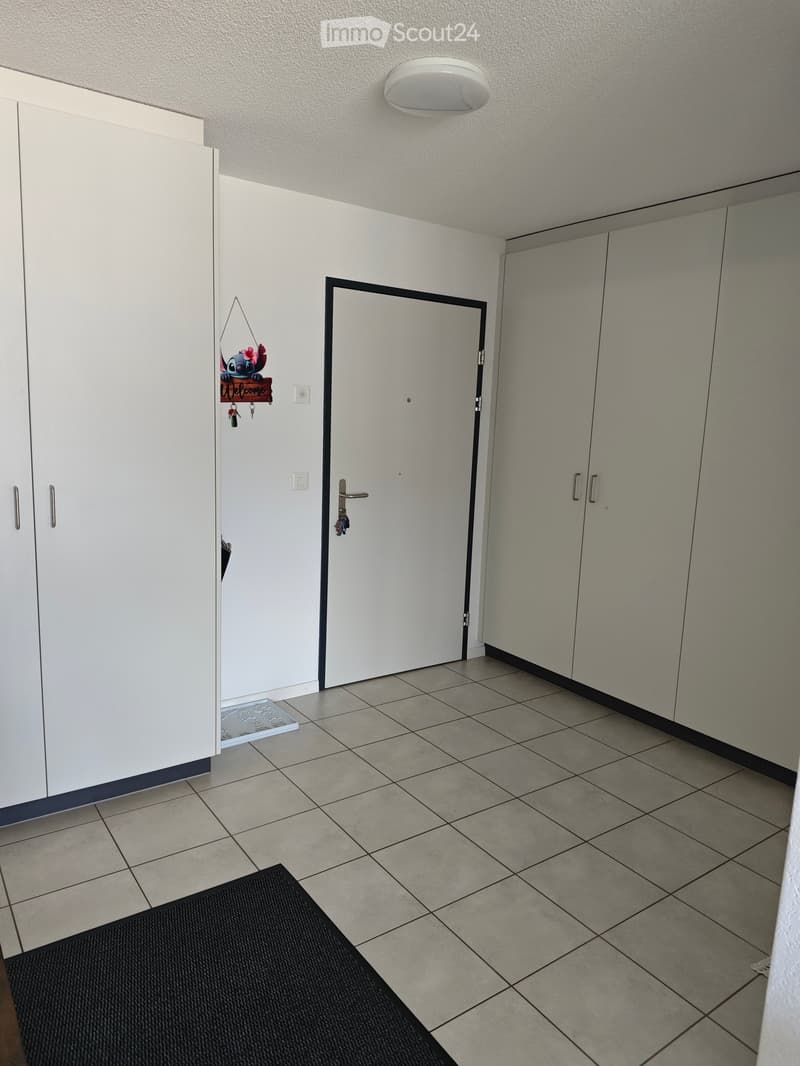 Empty hallway with tiled floor, white walls, built-in storage cabinets, and a closed door.