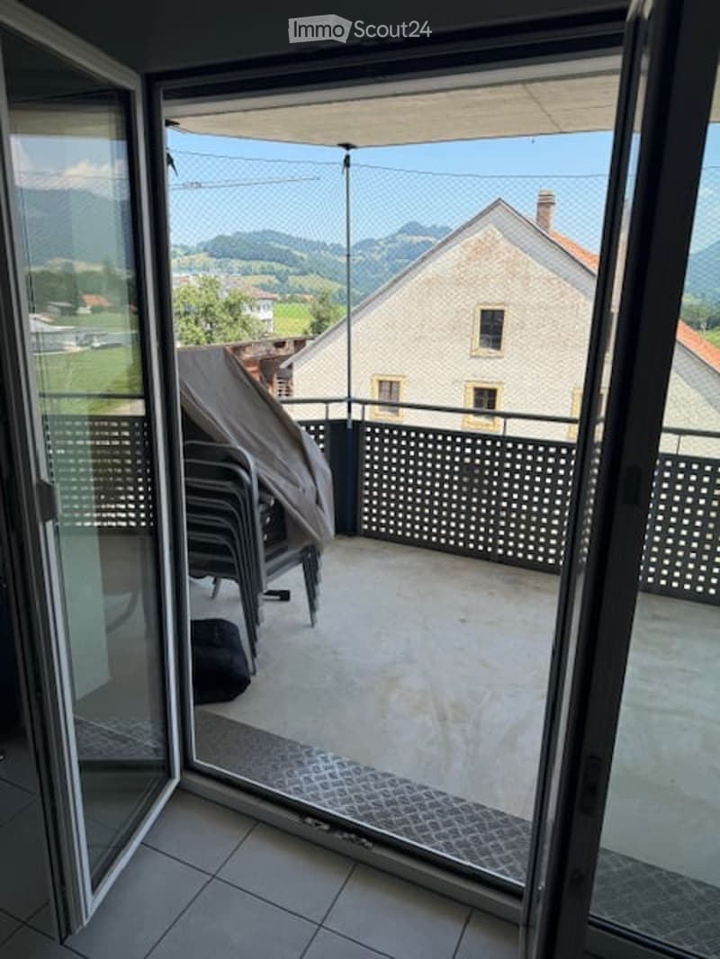 Balcony with a view of a rural landscape, featuring a covered chair and a black bag on the floor.