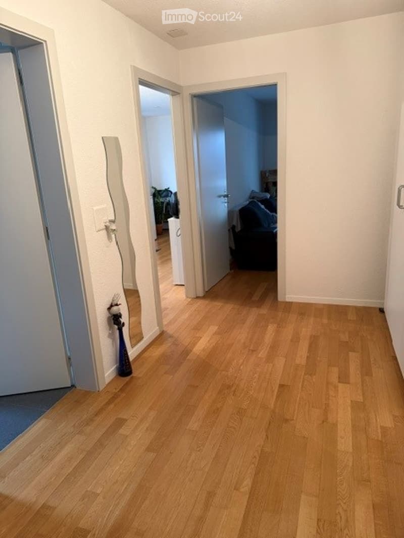 Empty hallway with wooden flooring, white walls, and multiple doors leading to other rooms.