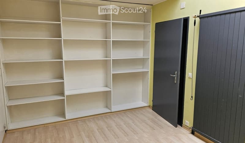Empty room with wooden flooring, white built-in shelving unit, and two closed doors.