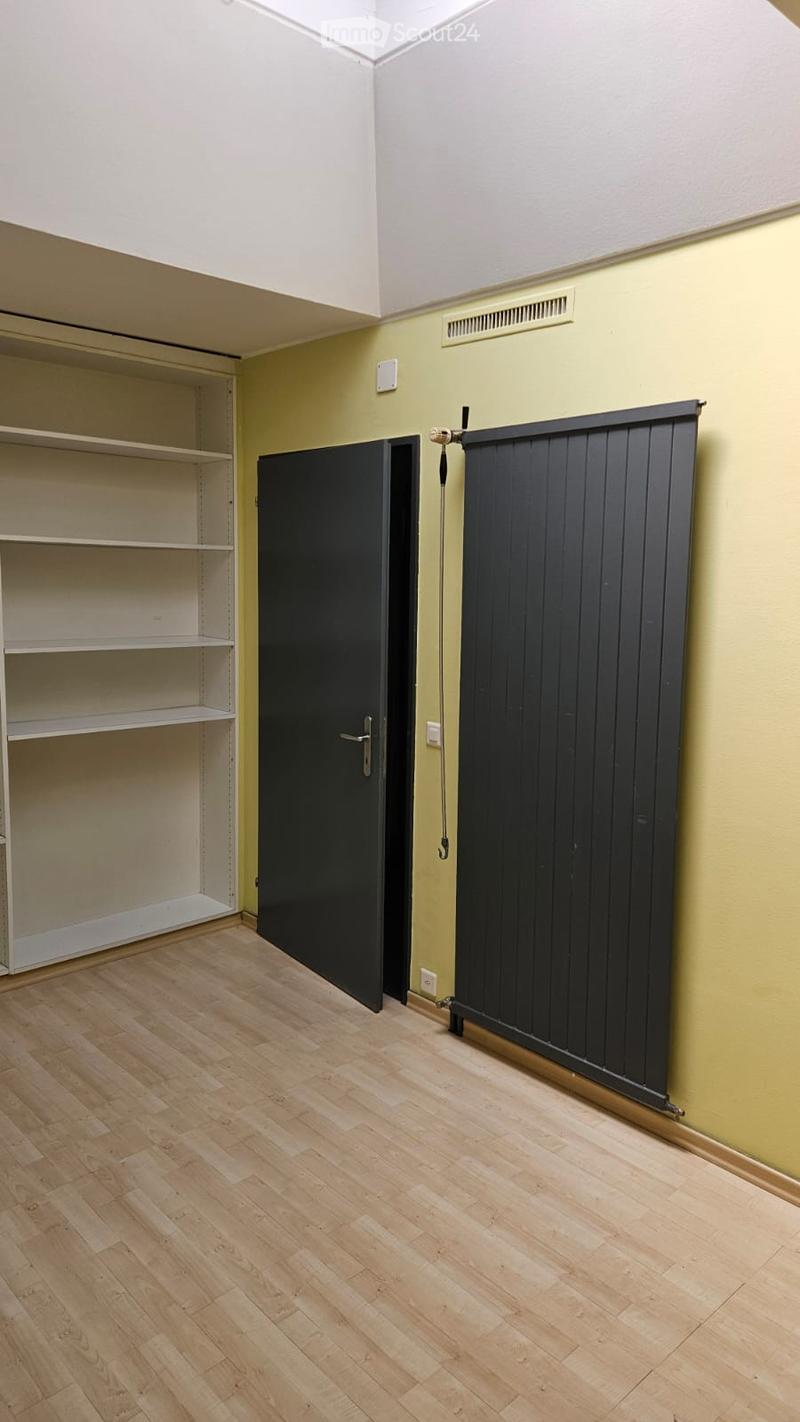 Empty room with wooden flooring, white walls, and built-in shelving unit. Features a closed black door and a partially open closet with empty shelves.