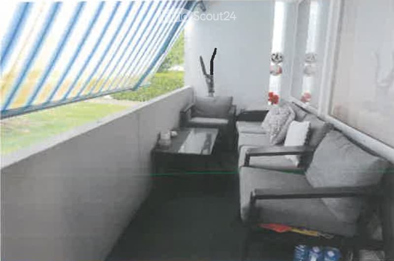 Balcony with grey sofa, coffee table, and striped awning, overlooking a green lawn.