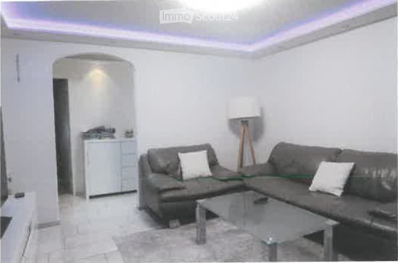 Modern living room with a grey sectional sofa, white throw pillows, a glass coffee table, a floor lamp, and a small white cabinet in the background.
