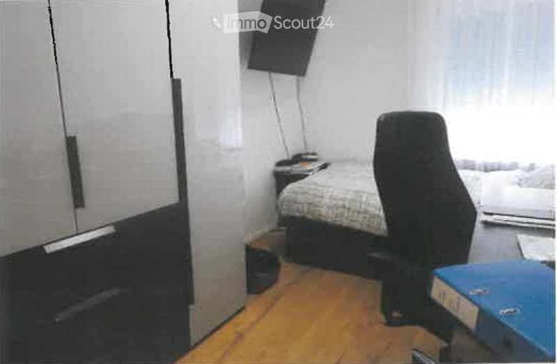 A small, furnished room with a bed, a chair, a wardrobe, a screen, and a table.