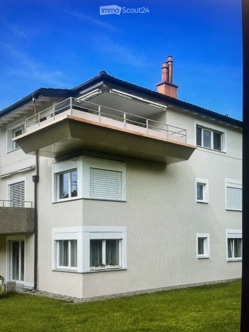 Modern two-story building with a balcony on the upper floor, white-framed windows, and a chimney.