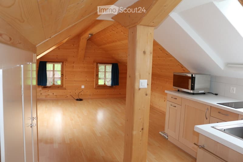 Bright, wooden kitchen with light wooden cabinets, a microwave, and a sink, featuring wooden floors and large windows.
